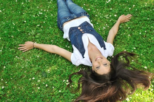 Young woman lying in fresh green grass with flowers - above view