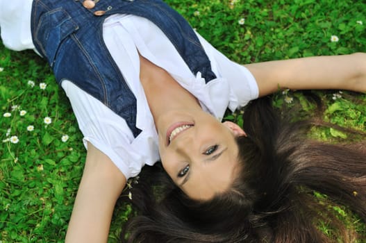 Detail of young woman lying in fresh green grass with flowers - above view