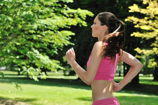 Young beautiful woman in pink running (jogging) outside in park on sunny day