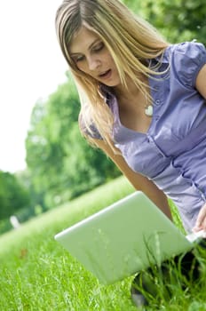 Young blond woman working with netbook outdoors in park on grass - surprise expression