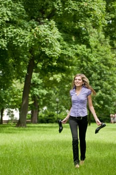 Young beautiful woman wit running in grass barefoot and holding shoes in hands