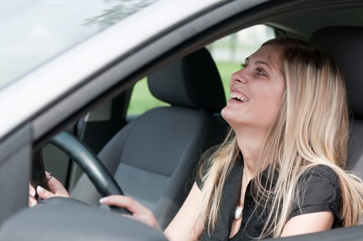 Young beautiful laughing woman driving car - portrait through side window