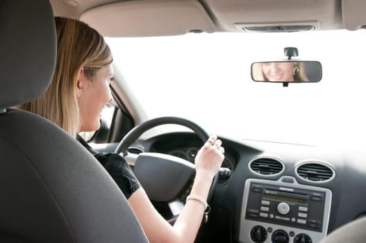 Young cheerful woman driving car - rear view, reflexion of mouth in mirror