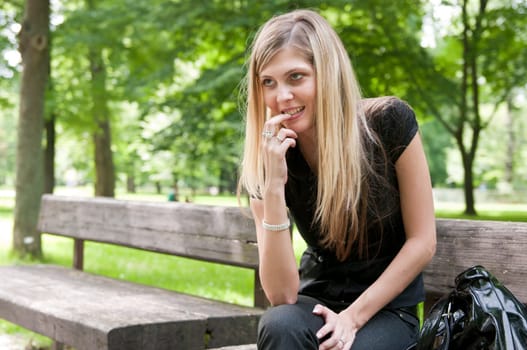Portrait of young beautiful flirting woman siting on bench in park outside