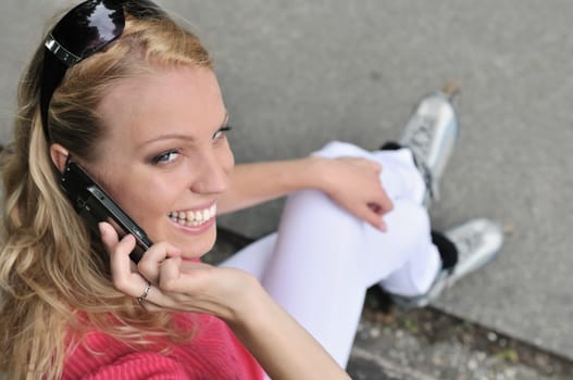 Young smiling woman wearing rollerblades calling with mobilephone outdoors
