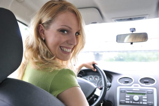 Portrait of young smiling woman siting behind steering wheel inside car