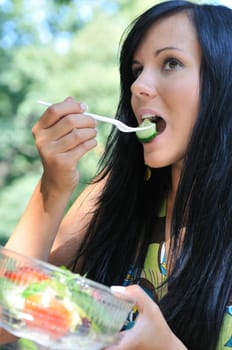 Young beautiful woman having lunch break and eating salad outdoors in park