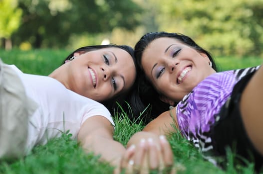 Togetherness - two smiling sisters lying in grass outdoors and holding hands, detail