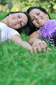 Togetherness - two smiling happy sisters lying in grass outdoors and holding hands with copy space