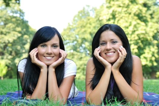 Frendship - two smiling friends lying happy together in park outdoors, hands under chin