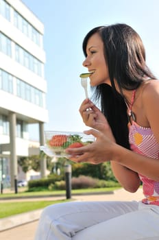 Young beautiful woman having lunch break and eating salad outdoors with building in background