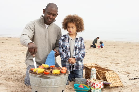 Young Family Enjoying Barbeque On Beach