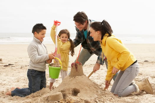 Family Building Sandcastle On Winter Beach