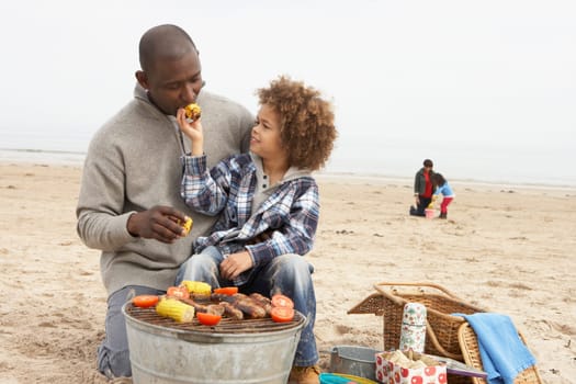 Young Family Enjoying Barbeque On Beach
