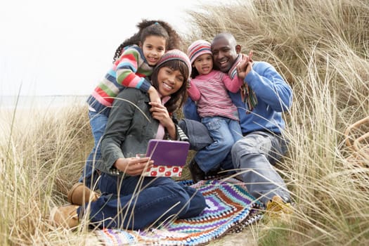 Family Sitting In Dunes Enjoying Picnic On Winter Beach