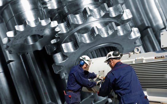 engineers, steel-workers, with giant gear wheels machinery, metal and steel works concept