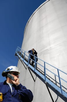 engineers talking to each other, large industrial fuel-storage tanks, shot inside refinery