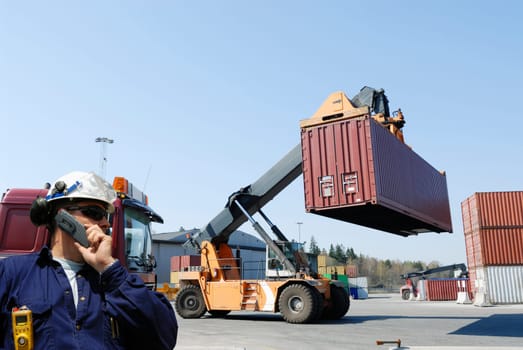 worker directing forklifts, stacking cargo-containers in a busy commercial container port