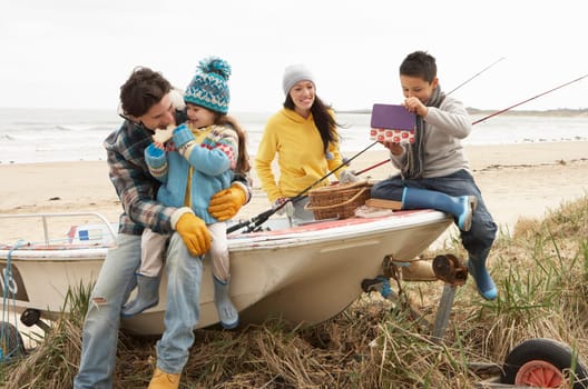 Family Group Sitting On Boat With Fishing Rod On Winter Beach