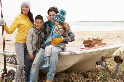 Family Group Sitting On Boat With Fishing Rod On Winter Beach