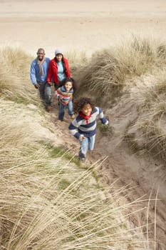 Family Walking Along Dunes On Winter Beach