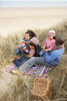 Family Sitting In Dunes Enjoying Picnic On Winter Beach
