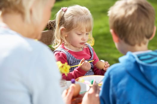 Mother And Children Decorating Easter Eggs On Table Outdoors