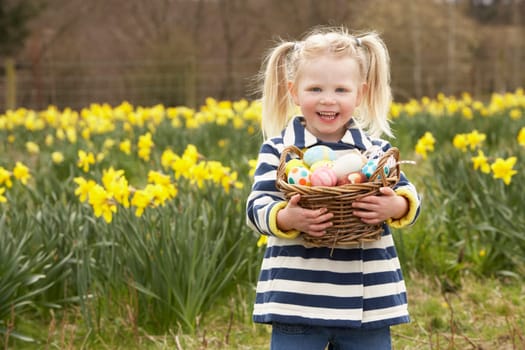 Young Girl Holding Basket Of Decorated Eggs In Daffodil Field