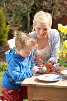Mother And Son Decorating Easter Eggs On Table Outdoors