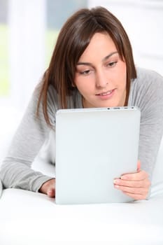 Young woman laying on sofa with electronic pad