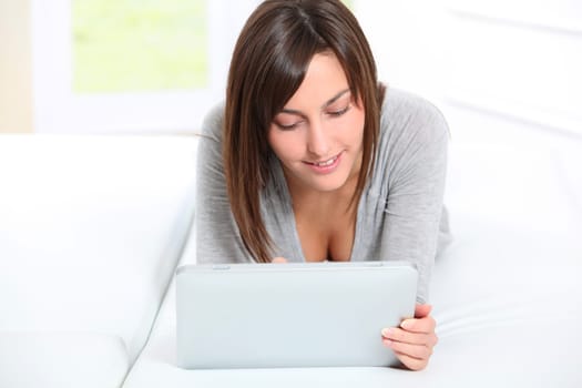 Young woman laying on sofa with electronic pad