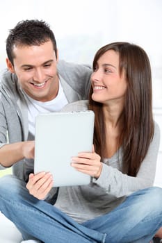 Young couple sitting on sofa with electronic pad