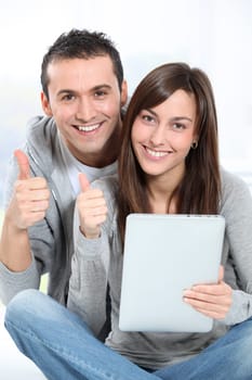 Young couple sitting on sofa with electronic pad