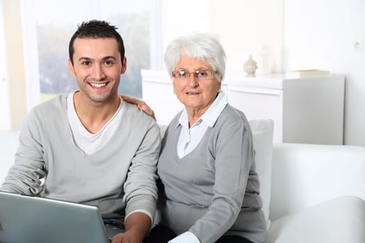 Elderly woman with young man using internet at home