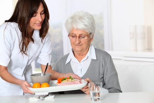 Beautiful nurse bringing meal tray to old woman at nursing home