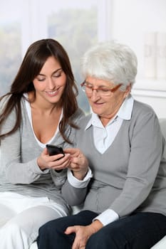 Young woman showing how to use mobile phone to grandmother