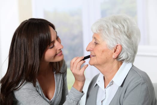 Young woman helping old woman to put makeup on