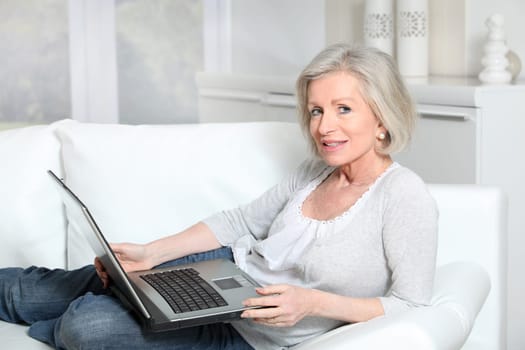 Senior woman sitting in sofa with laptop computer