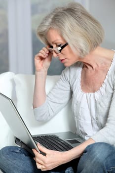 Senior woman sitting in sofa with laptop computer