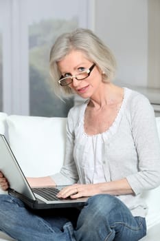 Senior woman sitting in sofa with laptop computer