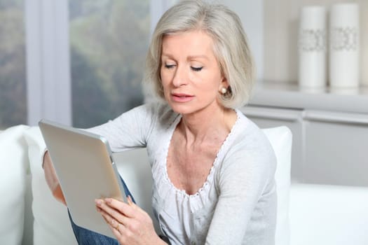 Closeup of senior woman sitting on sofa with electronic pad
