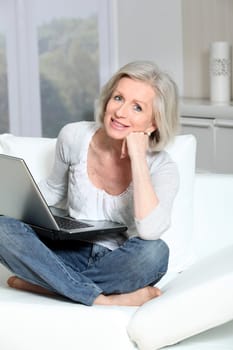 Senior woman sitting in sofa with laptop computer