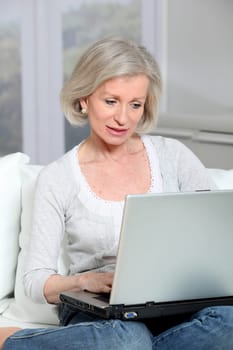 Senior woman sitting in sofa with laptop computer