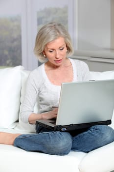 Senior woman sitting in sofa with laptop computer