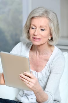 Closeup of senior woman sitting on sofa with electronic pad