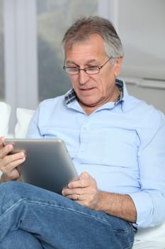 Senior man sitting in sofa with electronic tablet