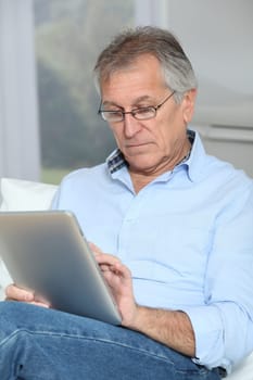 Senior man sitting in sofa with electronic tablet