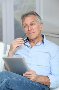 Senior man sitting in sofa with electronic tablet