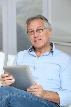 Senior man sitting in sofa with electronic tablet