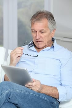Senior man sitting in sofa with electronic tablet